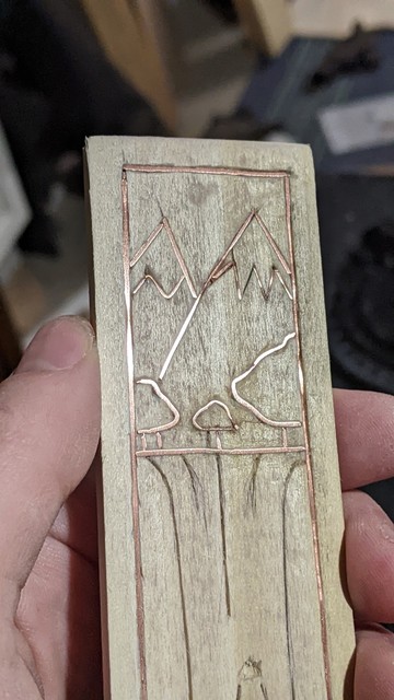 half finished wire inlay scene. Mountains, trees, a waterfall (evoking rivendell)