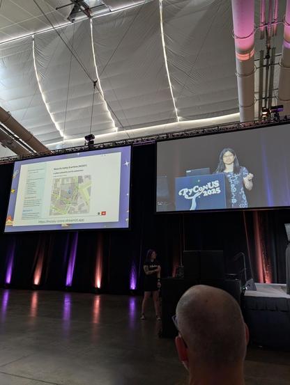 a stage backdrop: fay is on a screen on the right, on the left is a screenshot showing a map, and giving a "walkability score" and a number of car crashes. there is correlation.