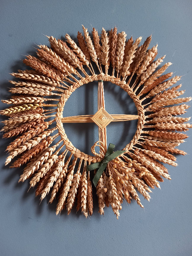 Wheat straw solar cross. The central component is like a Bridget's Cross but symmetrical, surrounded by a braided straw wreath from which heads of wheat project like solar rays.