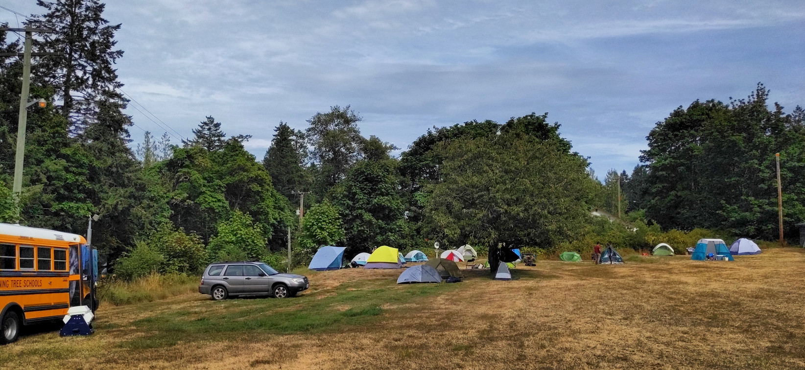 An open field with some camping tents and a yellow school bus.