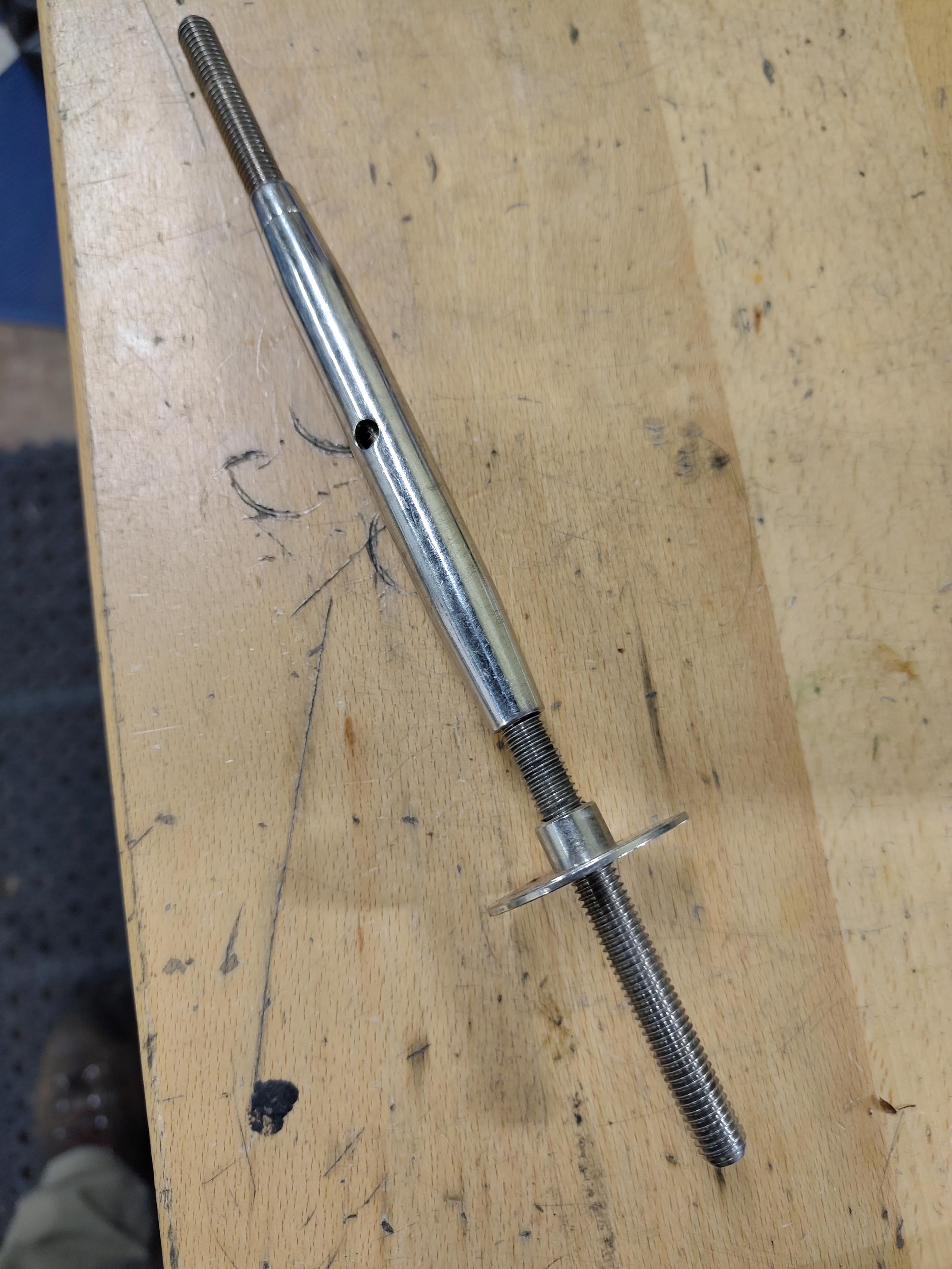 A long ovoid with a threaded rod sticking out at each end and a hole in the middle. On the longer of the two threaded rods is a bolt with a wide flat disc surface sticking off one side.