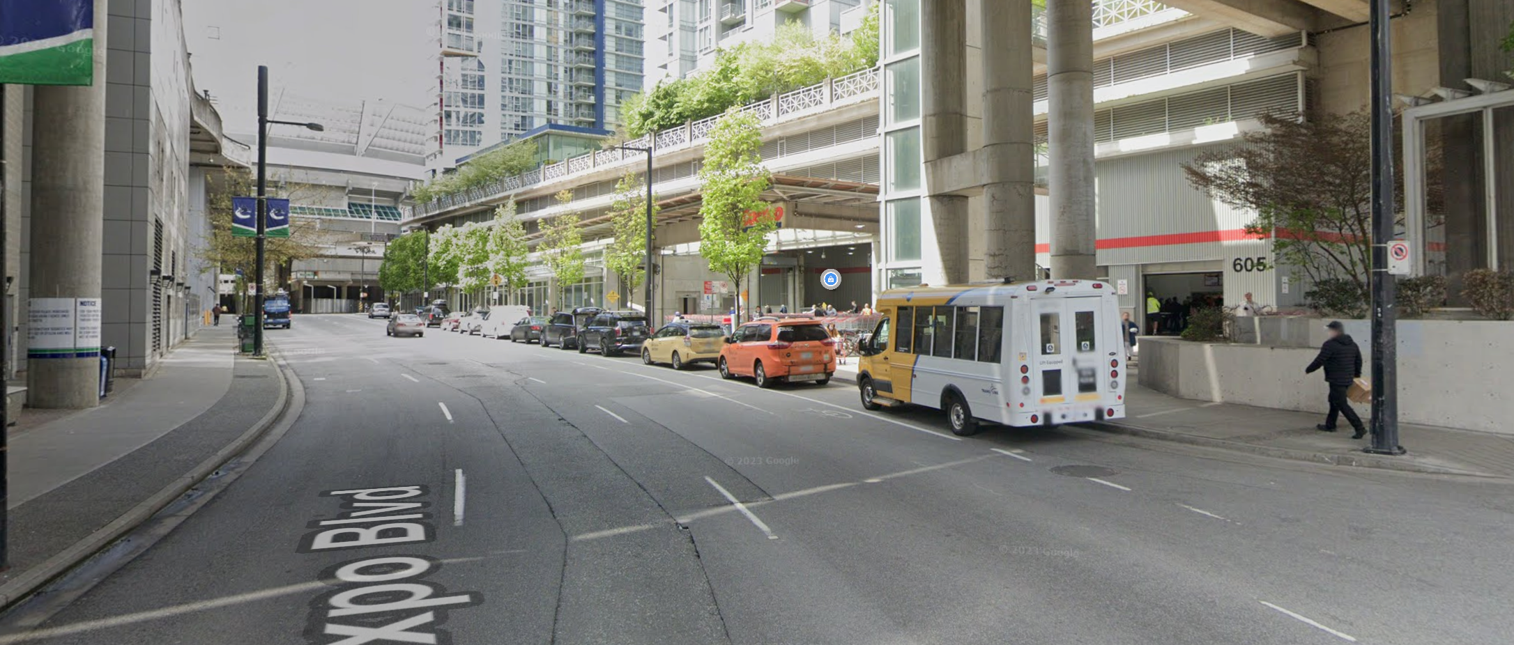 a wide one-way road consisting of 3 vehicle travel lanes, 1 bike lane, and a vehicle parking lane; the road is partly an urban concrete road tunnel with Costco on the bottom, and residential towers up top