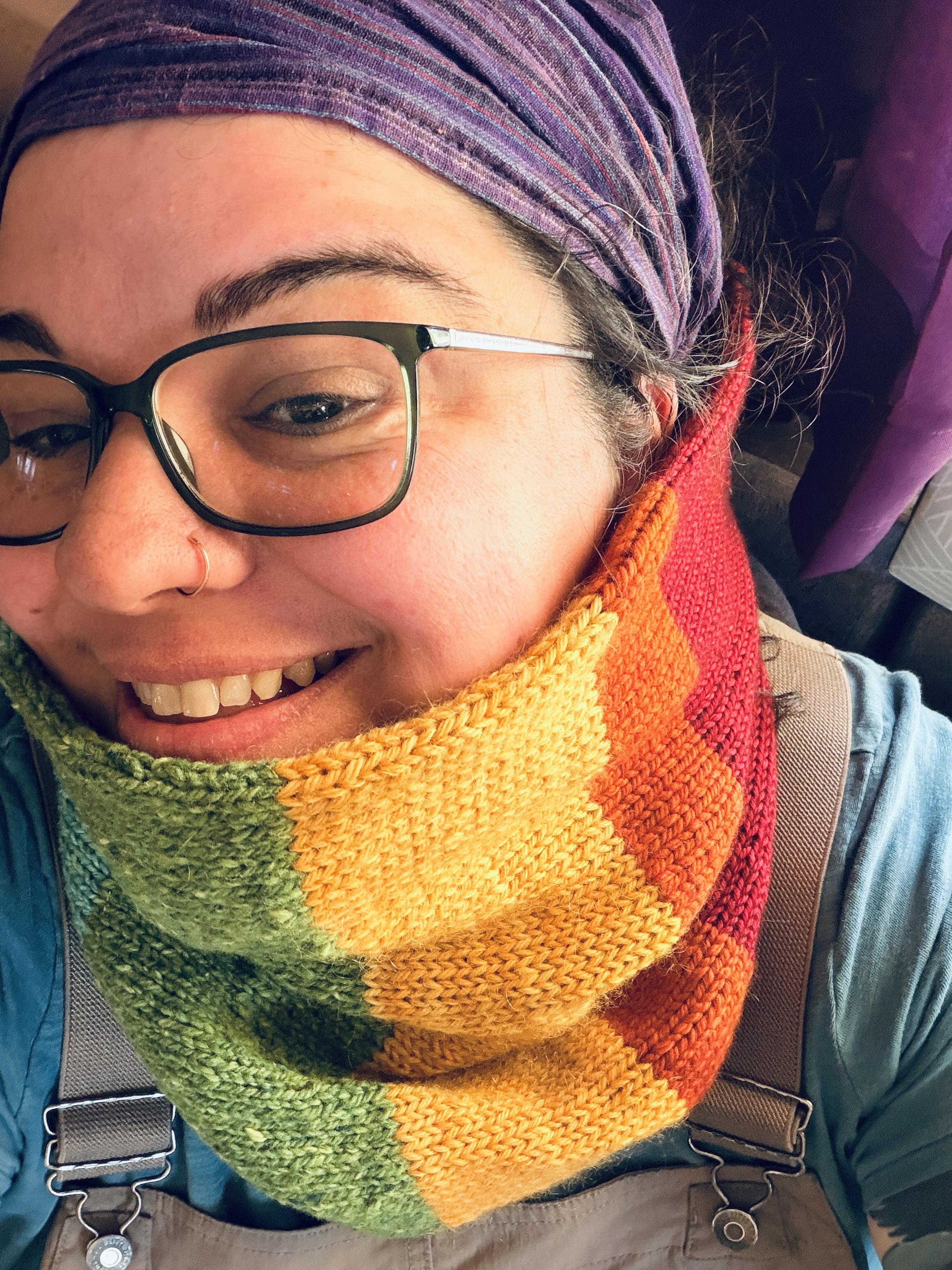 A total dorkball of a human is wearing a new rainbow cowl a friend hand knit for her. She is extremely happy about it.