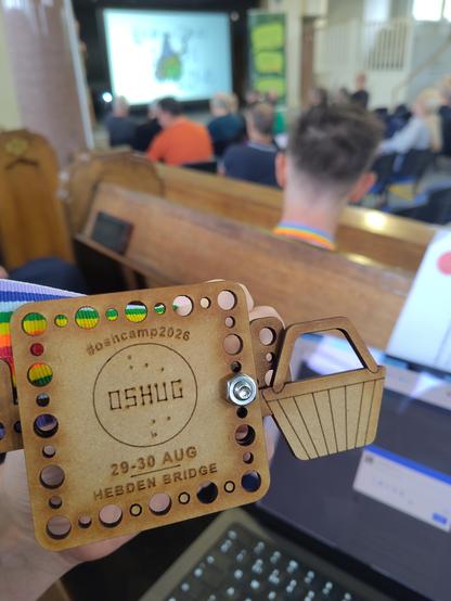 a lasercut customisable event badge in front of an out of focus scene of the backs of an audience enthralled by a speaker in a 19th century baptist chapel